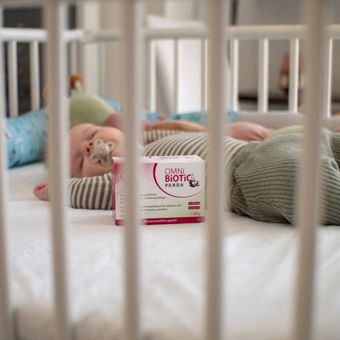 Eine Packung OMNi-BiOTiC PANDA neben einem schlafenden Baby